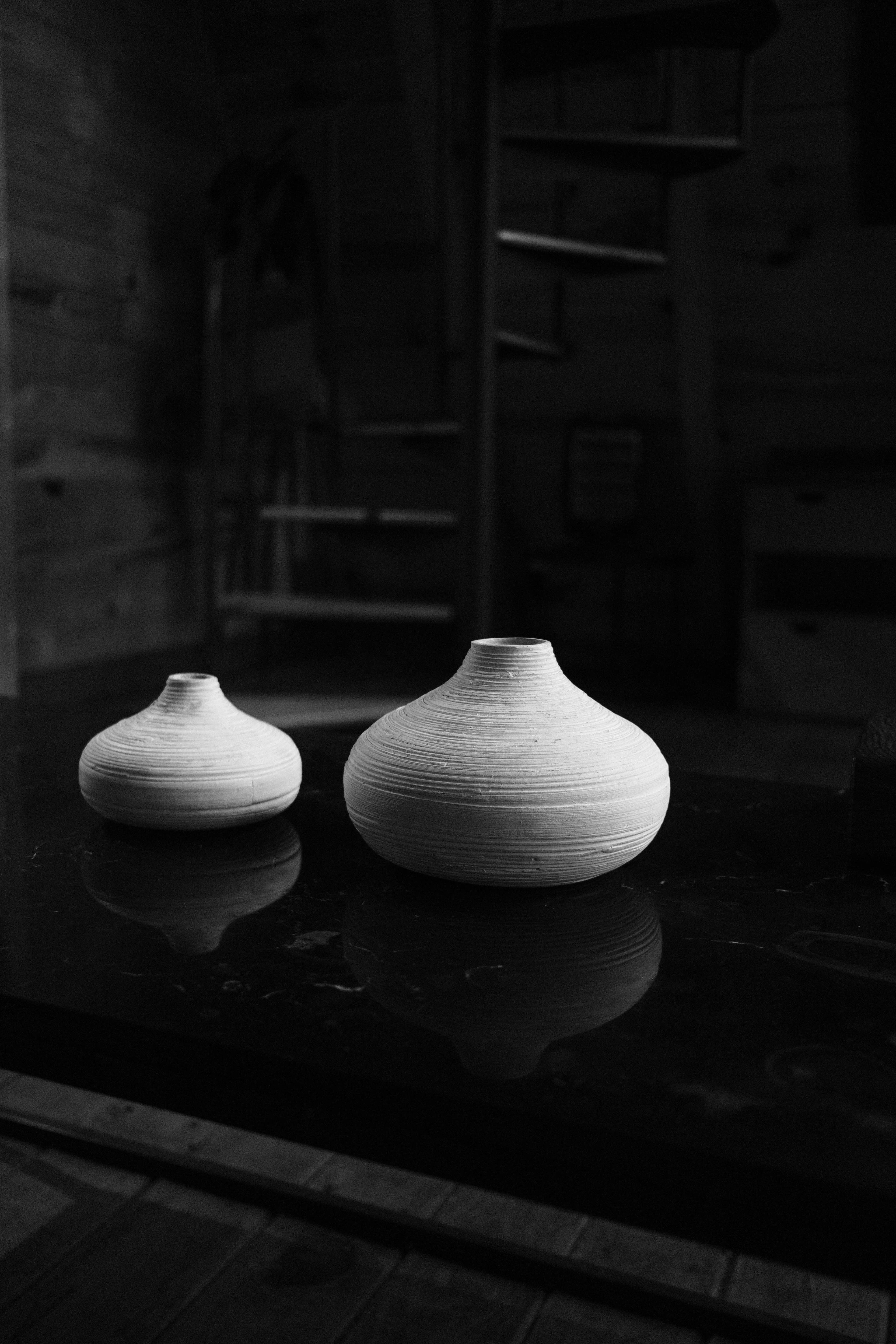 Black and white photo of two elegant ceramic vases on a wooden table in a rustic setting.