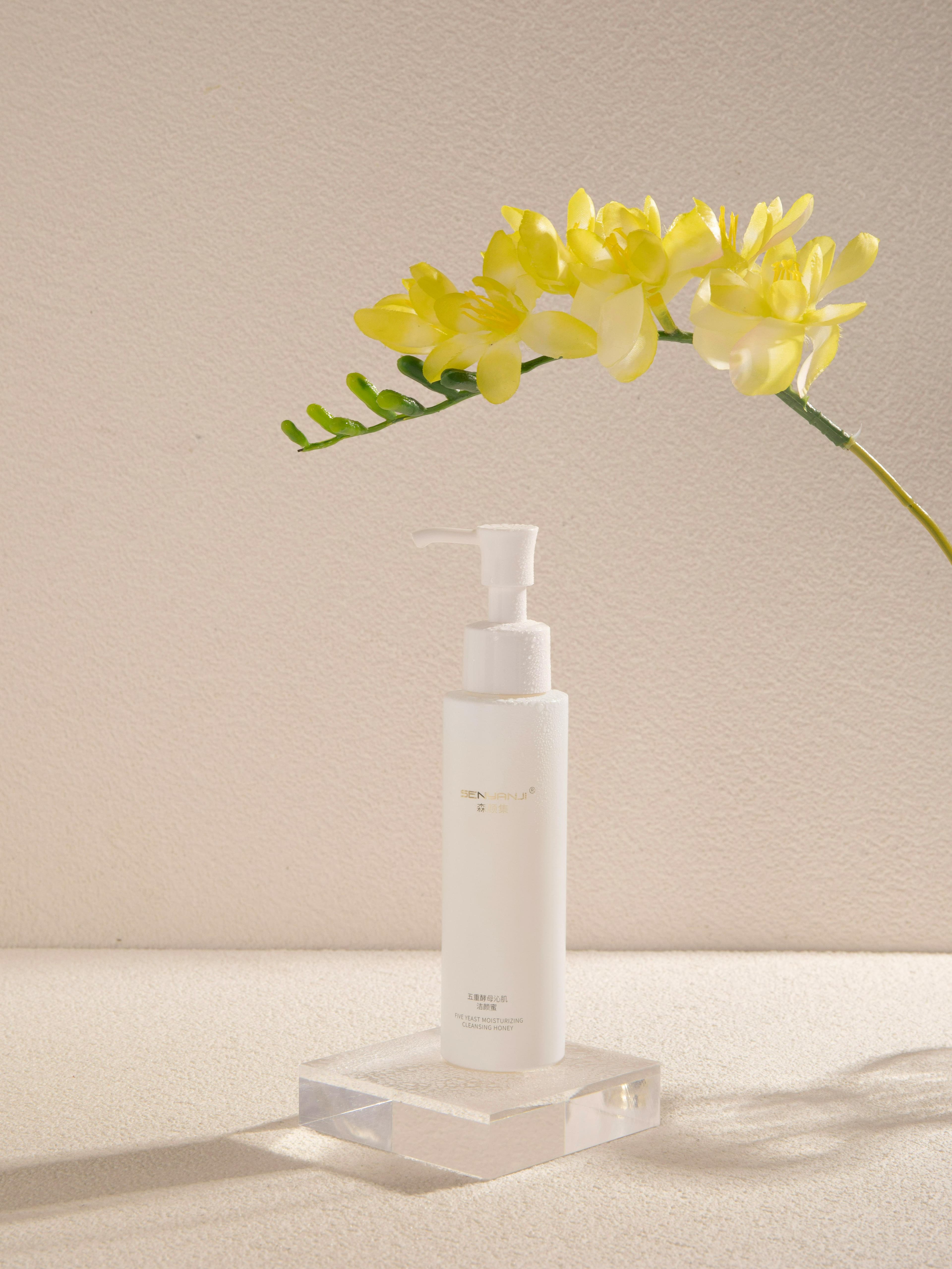 Minimalist skincare product display with yellow flowers on a white backdrop.