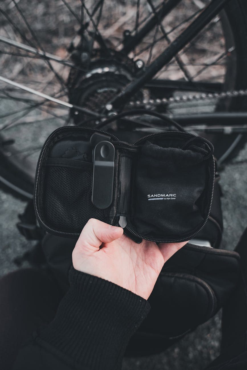 A hand holding an open Sandmarc camera accessory case near a bicycle wheel outdoors.