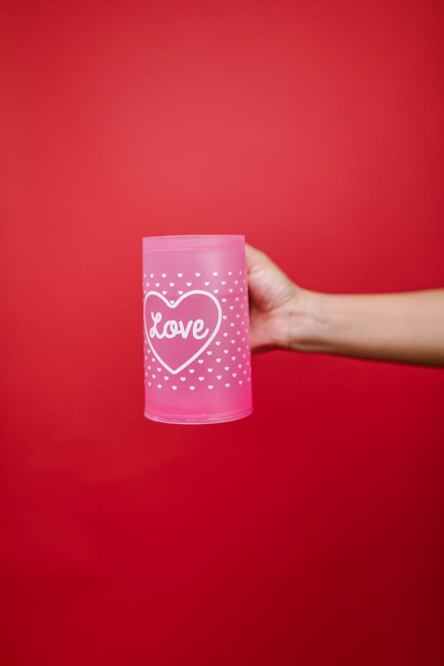 Pink mug with 'Love' text, perfect for Valentine's Day gifts, against a red backdrop.