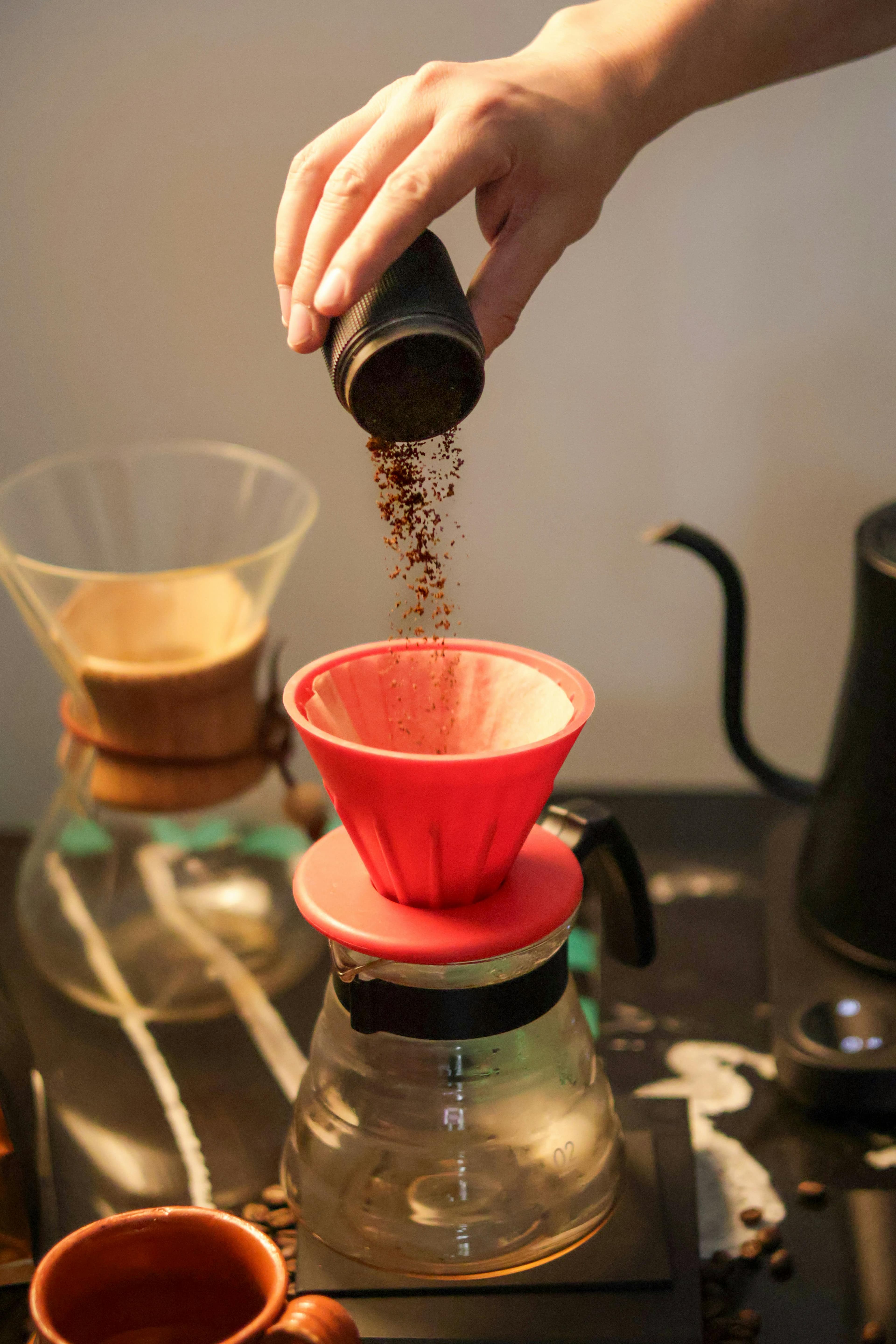 A hand carefully pours ground coffee into a vibrant red pour over filter, capturing the art of coffee making.