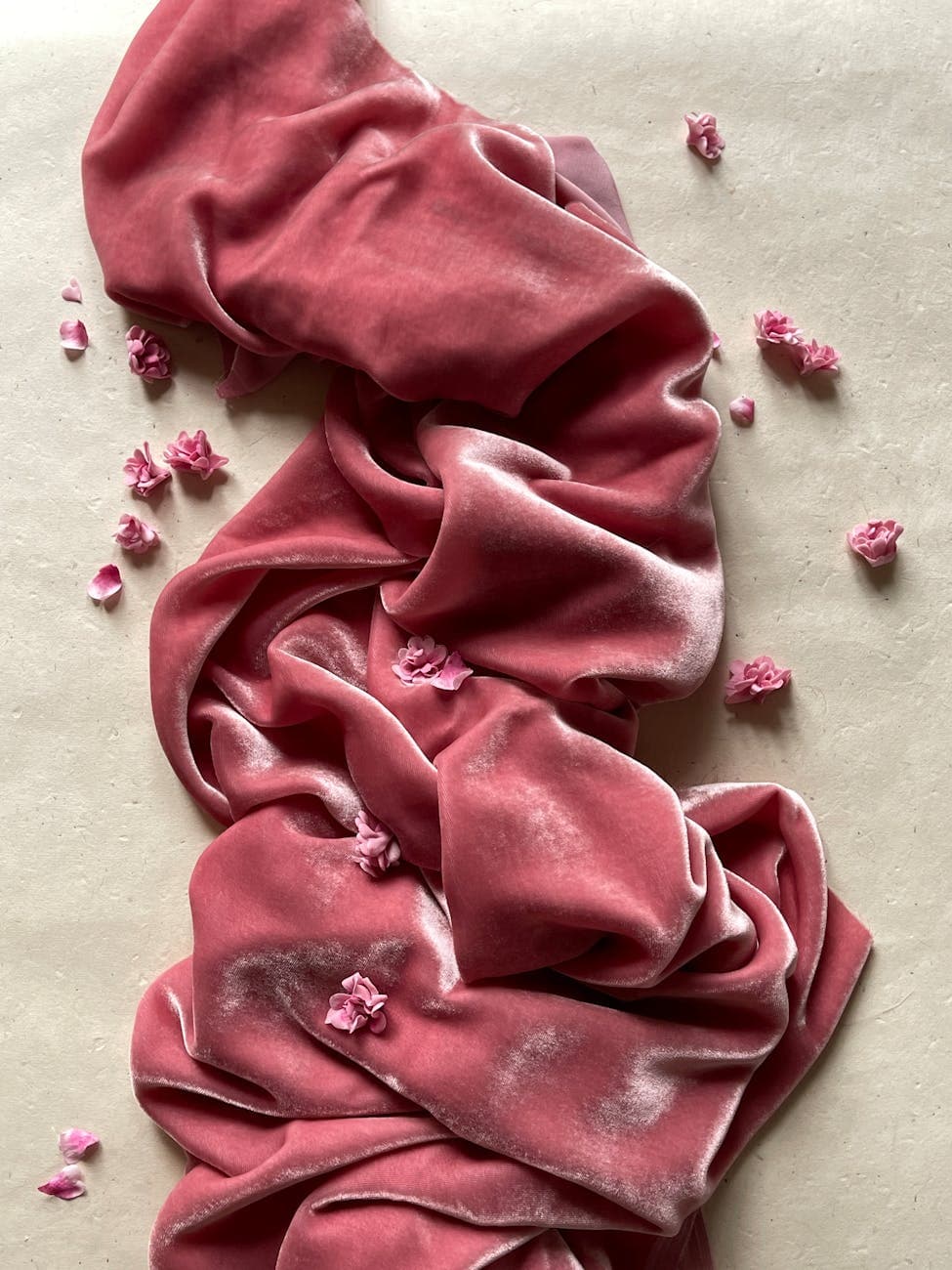 Luxurious pink velvet fabric draped with delicate flower petals, creating a romantic and elegant look.