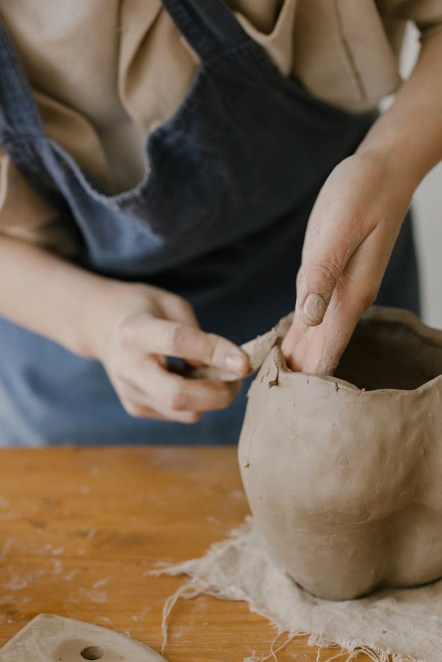 Close-up of a person skillfully shaping clay into a pot on a wooden table.