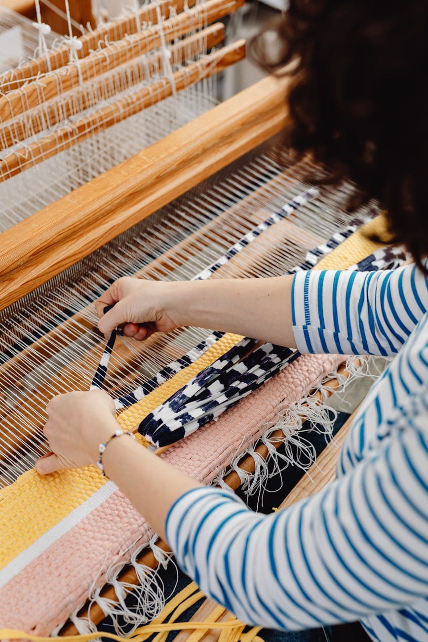 Hands weaving a colorful textile on a loom, showcasing craftsmanship and creativity.