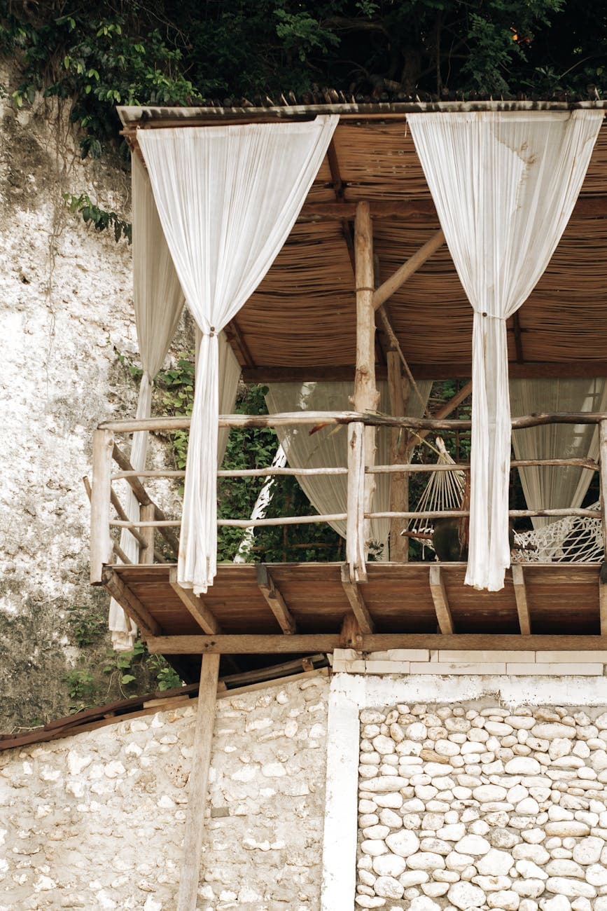 Beautiful rustic balcony with white curtains and hammock, perfect for relaxation.