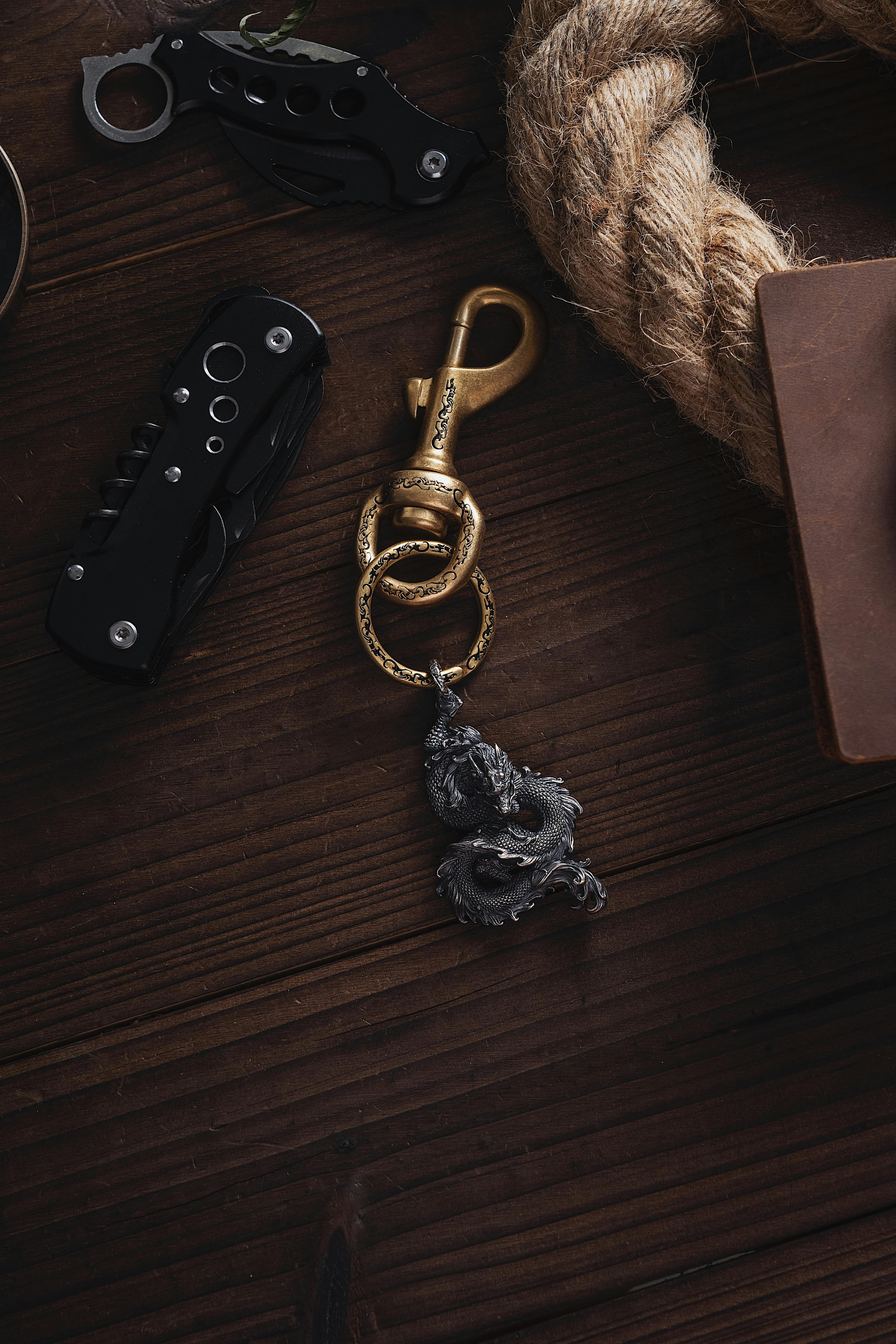 A dragon keychain with pocket knives and rope on a dark wooden surface.
