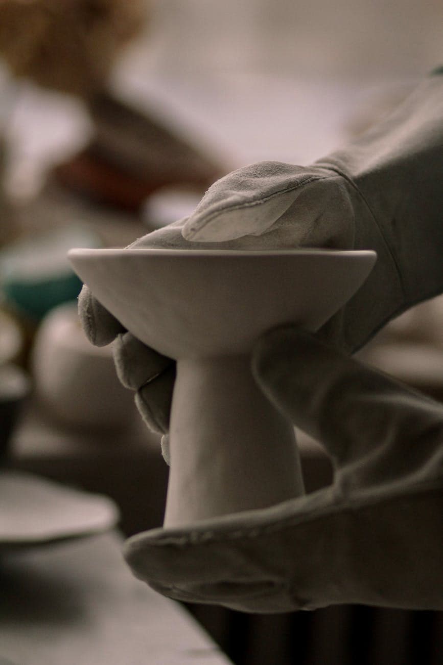 Gloved hands sculpting a ceramic piece in an artistic pottery workshop, showcasing craftsmanship.