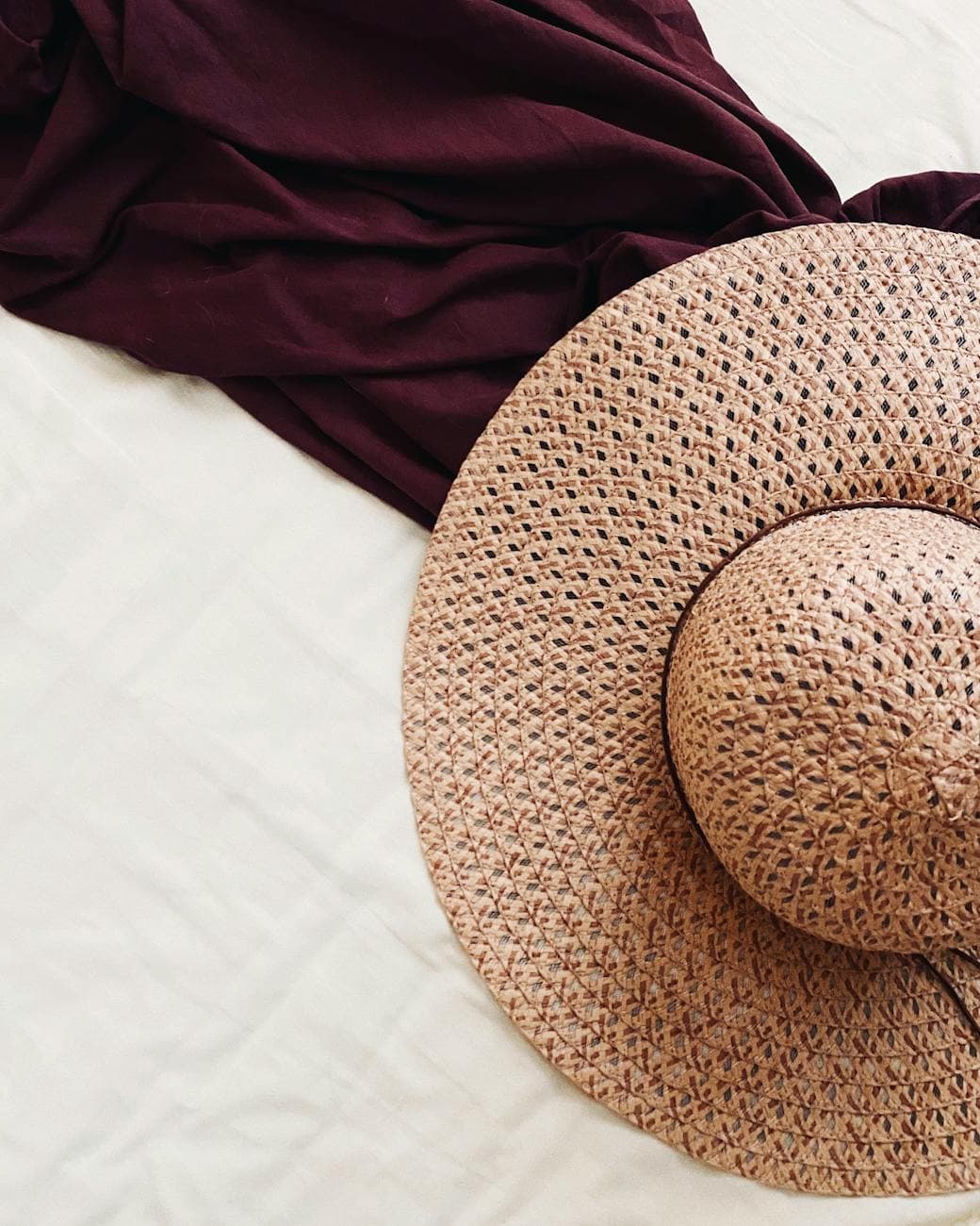 Close-up of a straw sun hat and fabric arranged on a light canvas, perfect for summer fashion themes.