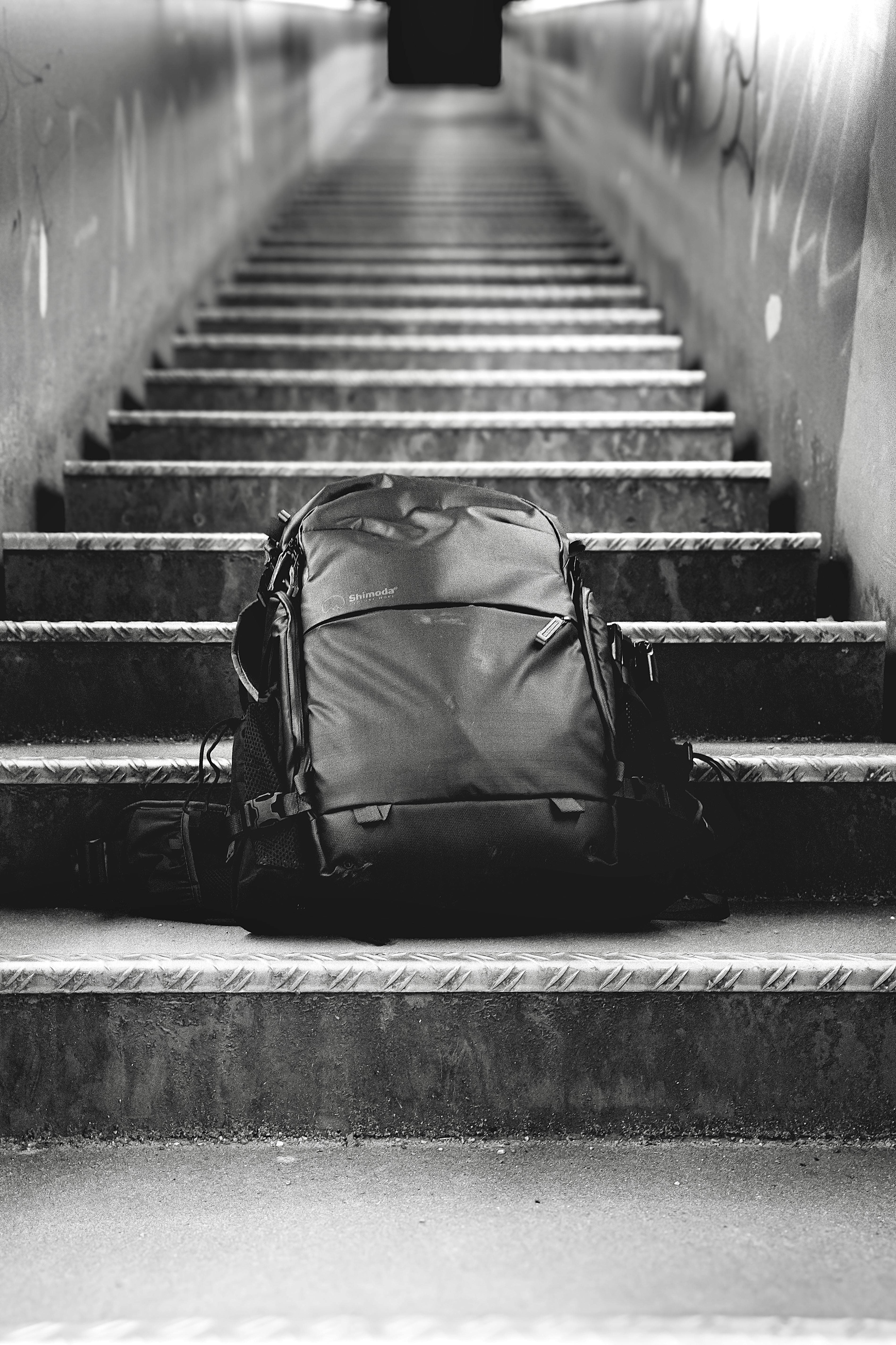 Black and white photo of backpack resting on urban staircase, emphasizing solitude.