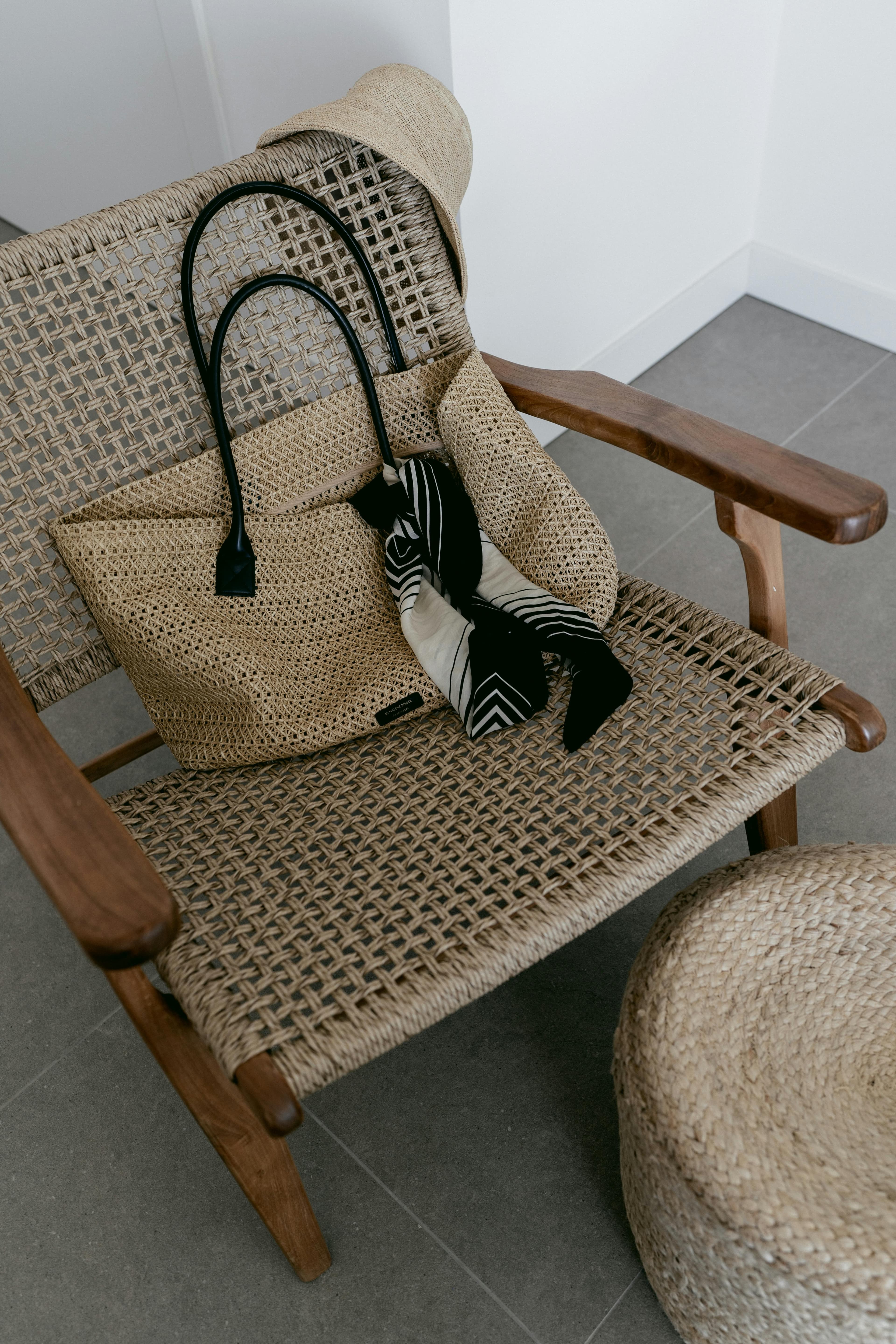 A wicker chair with a woven bag and scarf in a minimalist indoor setting, showcasing natural textures.